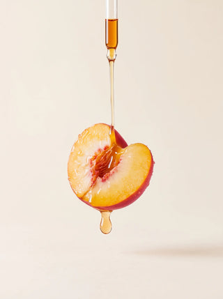 Drop of golden oil falling from a dropper onto a ripe peach half